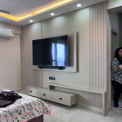 A modern bedroom TV unit with fluted paneling and a floating console. The design incorporates both open shelves and closed drawers for versatile storage.
