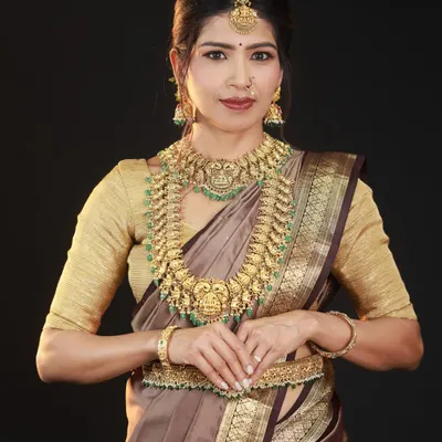 A classic portrait against a solid black background. This setup is perfect for making the intricate details of the antique-finish temple jewellery and the sheen of the silk saree pop.