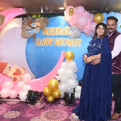 A beautiful portrait of the expecting couple in front of their "Mehra's Baby Shower" decor, featuring a moon and balloon theme.