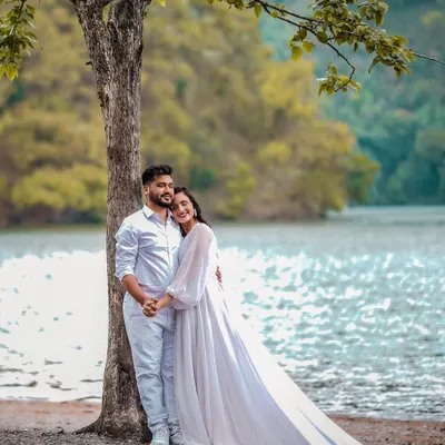 A serene pre-wedding photo of a couple by a lakeside in Uttarakhand. The flowing white dress and natural backdrop create a romantic, ethereal feel, perfect for a destination pre-wedding album.