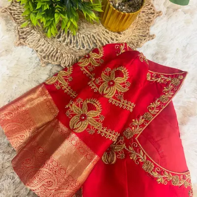 A close up of a bridal red blouse sleeve, showcasing dense floral embroidery in gold thread. The design combines traditional motifs with a modern aesthetic, perfect for a wedding saree.
