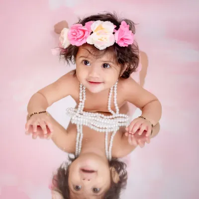 This is a perfect example of a sitter session, capturing the baby's joyful expression and curiosity. Using a mirror creates a playful and unique composition, reflecting her happy smile and celebrating this fun stage of development.