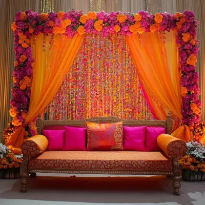 For a rich and royal mehendi, this setup combines a dense frame of bougainvillea-style flowers with shimmering gota patti curtains and a classic diwan.