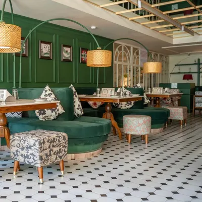 A full view of the custom furniture I created for "The Drawing Room" at Smoke House Deli. The setup includes curved green velvet banquettes, dining tables, and uniquely upholstered ottomans, all designed to fit the whimsical theme of the space.