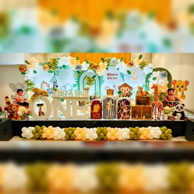 A full view of our 'Wild One' jungle safari theme, perfect for a first birthday. The stage includes a large backdrop, animal-print plinths, character cutout's of a lion, monkey, and giraffe, and a balloon garland in natural green's and white's.