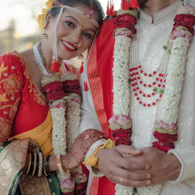 A radiant Maharashtrian bride rests her head on her groom's shoulder. This close-up highlights her beautiful smile, traditional nath, and the intricate details of their wedding garlands.