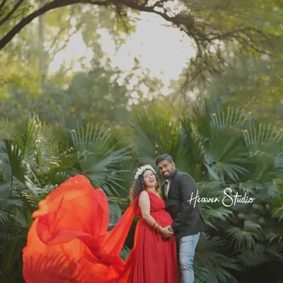 A beautiful portrait of a couple celebrating their love amidst nature. The vibrant red of her gown creates a stunning contrast with the lush greenery, making for a truly memorable outdoor maternity photo.