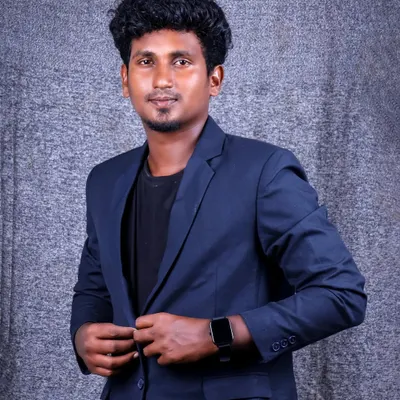 A sharp and modern men's portrait. The subject is wearing a navy blue blazer over a black t-shirt, creating a smart-casual look against a textured grey studio backdrop.