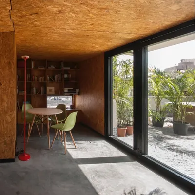 A small workspace we designed for a journalist, seen from the terrace. The use of OSB wood for all interior surfaces creates a warm, monolithic feel, while the large glass opening connects the office to the outdoors.
