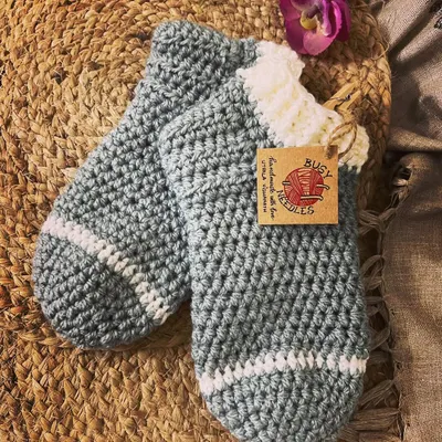 Keep your feet warm and cozy with these handmade crochet socks. This pair in grey and white is perfect for lounging at home on a cold night.