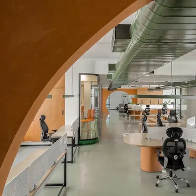 An arched entryway frames the view into the open-plan office we designed for Hosachiguru. The color palette of terracotta and forest green, along with exposed ducting, reflects the company's focus on sustainable farming and technology.