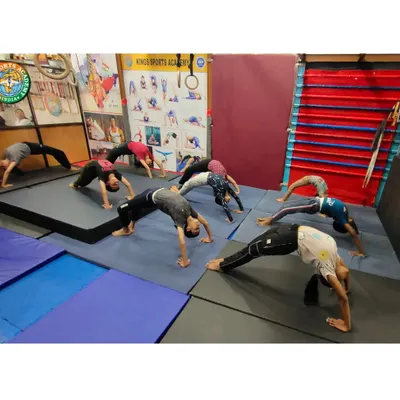 A look inside our group classes where students work on flexibility and back strength. Here, a group practices Chakrasana, or the wheel pose, on padded mats, showing the focused and disciplined environment of our academy.