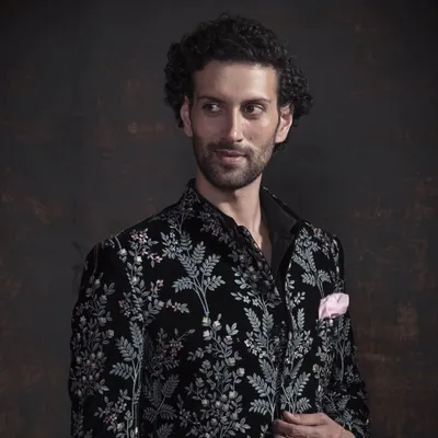 A close-up of the black velvet bandhgala with intricate silver floral embroidery. The craftsmanship is designed to be appreciated up close, showcasing the texture and detail.