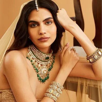 A stunning bridal look for Carbon Jewellery, featuring a warm, bronzed smokey eye and a neutral lip. The makeup enhances the model's features while complementing the heavy polki and emerald necklace.