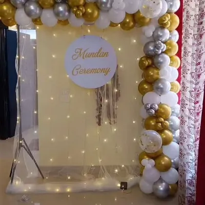 An elegant and modern Mundan ceremony backdrop. This setup features a white and gold balloon frame, a personalized sign, and a delicate curtain of fairy lights.
