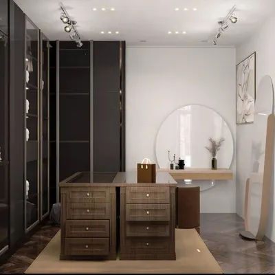 A spacious walk-in closet featuring dark, sleek wardrobes and a central island with drawers for accessories. The large round mirror and separate vanity area create a dedicated and luxurious dressing space.