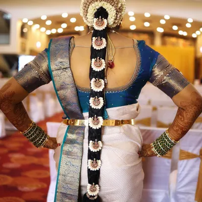 A classic South Indian bridal braid, or Poola Jada. This hairstyle features a neat braid adorned with jasmine flowers and traditional billai ornaments, creating a timeless and elegant look from the back.