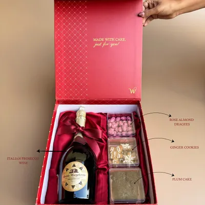 A detailed look inside my Signature Box 2.0. This annotated image shows the curated selection of Italian Prosecco, rose almond dragees, ginger cookies, and plum cake.
