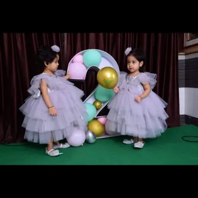 Twin sisters celebrating their second birthday in identical lavender layered gowns. These frocks are designed with soft tulle and flutter sleeves, making them perfect for little ones.