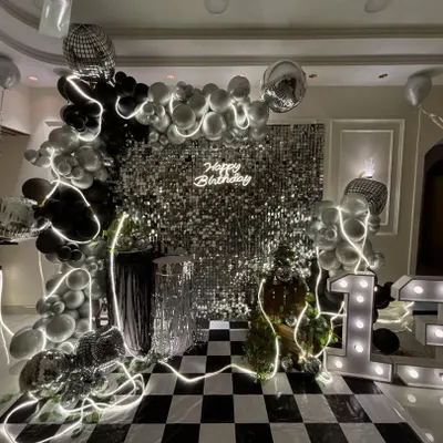 The centerpiece of a 13th birthday bash, this setup combines a silver shimmer wall, a neon 'Happy Birthday' sign, and a black and silver balloon arch. The marquee '13' and checkered floor complete the high-energy disco theme.