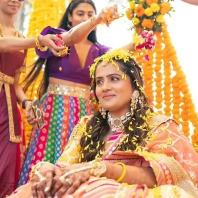 A beautiful moment from a Haldi ceremony. The bride is showered with flowers, and her makeup is kept fresh and minimal to let her natural glow shine through.