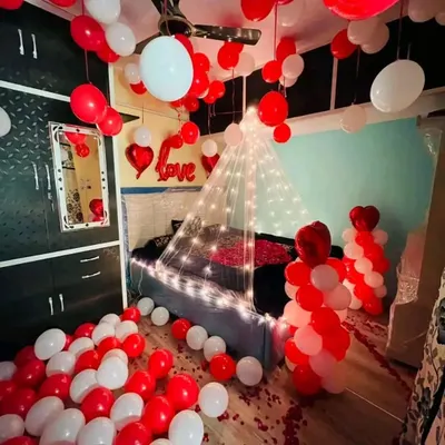 A classic red and white themed room decoration. The space is filled with balloons on the floor and ceiling, with a fairy light canopy over the bed and 'Love' foil balloons to complete the romantic surprise.