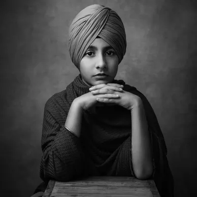 A powerful and poised portrait of a young boy. The black and white format emphasizes his strong gaze and the beautiful details of his turban, creating a timeless and striking image.