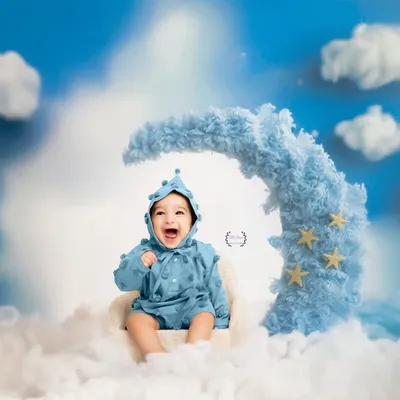 Over the moon with happiness! This adorable baby is all smiles, sitting on a fluffy blue crescent moon surrounded by clouds and stars. It's a truly dreamy and joyful setup.