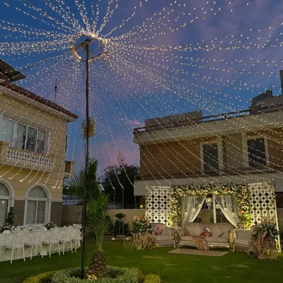 A stunning outdoor setup for an anniversary celebration at dusk. The canopy of lights, elegant seating, and floral stage create a truly magical and romantic atmosphere.