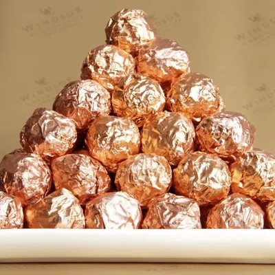 A pyramid of our signature NOCOCHOCO hazelnut truffles. Each one is a sphere of creamy milk chocolate and crunchy wafer surrounding a whole toasted hazelnut, all wrapped in a beautiful rose gold foil.