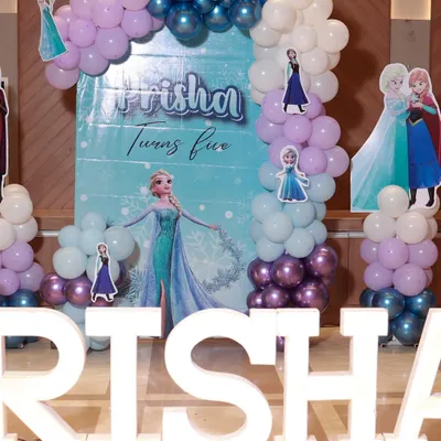 A magical Frozen-themed party for Prisha's fifth birthday. The backdrop features Elsa and Anna, framed by a balloon arch in icy shades of blue, purple, and white, with large marquee letters in the front.