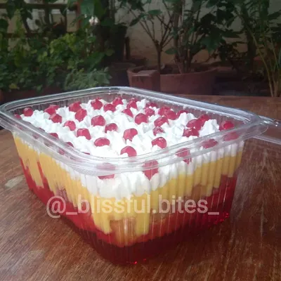 My Mixed Fruit Trifle in a party-sized container, showing the distinct layers of red jelly, yellow custard, and white cream, topped with pomegranate seeds.