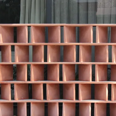 A close-up of the red sandstone jali from the Jaipur House. Each block is angled to filter the harsh sun while allowing for ventilation, a modern interpretation of a traditional Rajasthani architectural element.