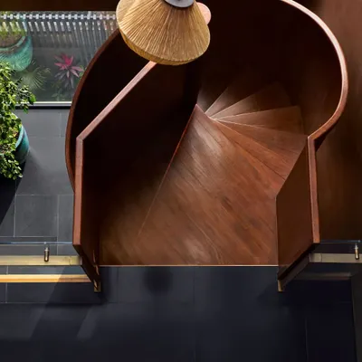An overhead view of the spiral staircase at the Urban Hearth residence. Crafted in matte black metal and polished wood, its form is a gentle, turning ascent that anchors the double-height space while maintaining a sense of lightness and air.