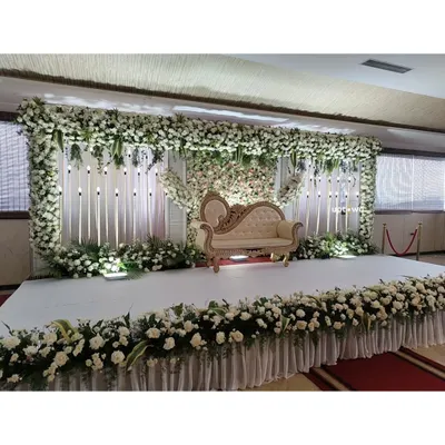 A classic and elegant all-white floral stage for a reception or engagement. The dense flower wall and classic sofa create a timeless look.
