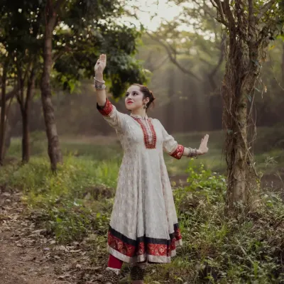 A full-length portrait of a Kathak dancer in a classic pose. The forest setting with rays of light filtering through the trees adds a magical quality to this performance portrait.