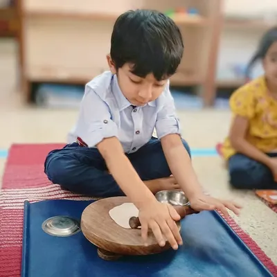 A child practices rolling dough, a practical life activity that strengthens hand and wrist muscles, preparing them for writing. This is also a wonderful sensory experience that builds coordination and focus.