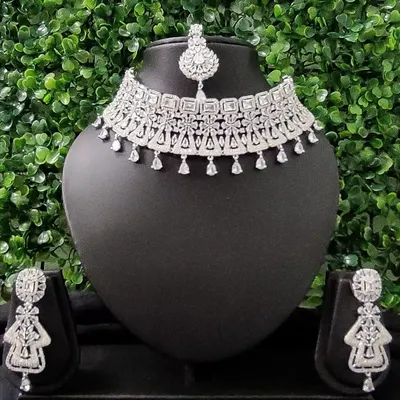 For the modern bride who loves to sparkle, this complete American diamond necklace set is a perfect choice for a reception or cocktail event. It includes a choker, matching earrings, and a delicate maang tikka.
