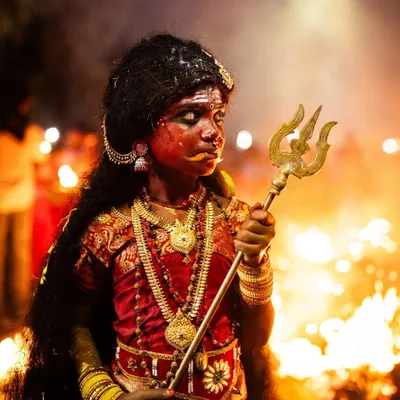 A young girl embodying the goddess Kali during the Kulasai Dasara festival. Her powerful expression and the fiery background create a portrait of fierce, divine energy.