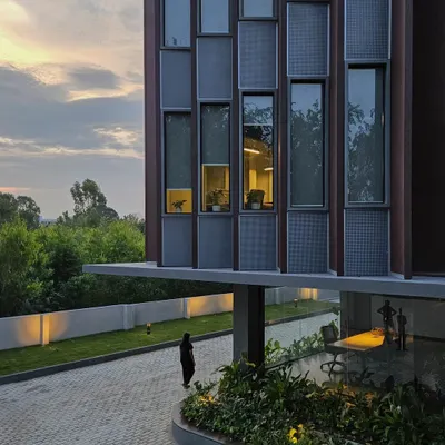 The building's facade at dusk, highlighting the interplay between the cantilevered entrance canopy and the gridded window pattern. This view shows how we integrate landscape and lighting to enhance the architectural form.
