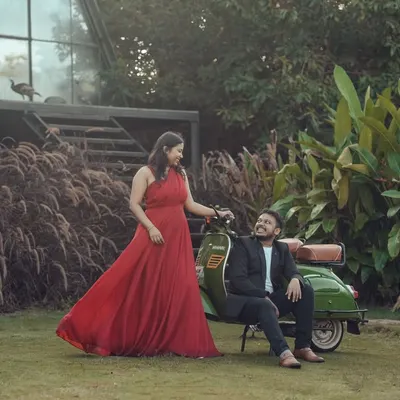 A couple poses with the vintage scooter in the garden. The vibrant red of the gown stands out against the green lawn and plants, showing how the space is perfect for colorful, lively photoshoots.