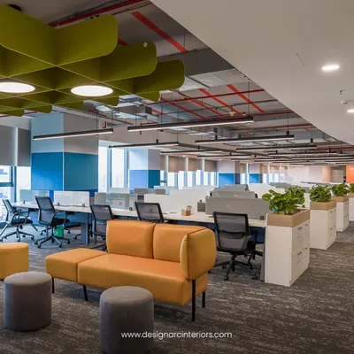 This open-plan office features bench-style workstations that promote teamwork, complemented by a comfortable lounge area for informal discussions. The design uses natural materials and plants to create a warm and productive atmosphere.