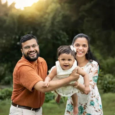 A happy family plays together in a park, with the parents lifting their daughter in the air. The golden hour sunlight creates a warm, magical glow.