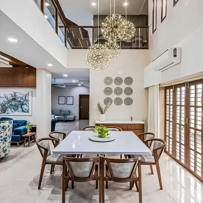 A bright and airy dining space in a double-height room. The modern wooden dining set is beautifully illuminated by a cluster of stunning spherical chandeliers.