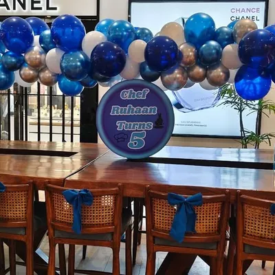 A simple yet cheerful balloon garland in shades of blue and silver, hung over a long table for a 5th birthday celebration.