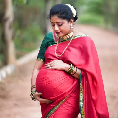 An absolutely stunning outdoor portrait of a mom-to-be in a traditional red and green silk saree. The way she holds her baby bump is so full of love and grace.