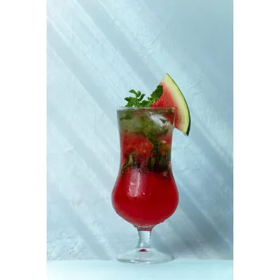 A bright, high-key shot of a watermelon mojito mocktail, garnished with fresh mint and a fruit slice. The clean, light background makes the drink's red color pop, creating a refreshing summer visual.