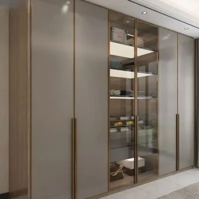 An elegant floor-to-ceiling wardrobe design. It features a mix of matte grey shutters and glass doors with a sleek metal frame, allowing for both concealed and visible storage.