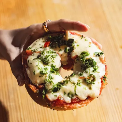 The best of both worlds: our signature Pizza Bagel. This one features a generous topping of cheese and herbs on a freshly baked bagel, perfect for a snack or light meal.
