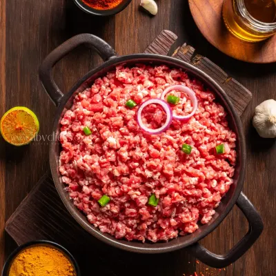 A top-down shot of fresh minced mutton in a cast-iron pot, surrounded by spices like turmeric and chili powder, creating a rich and rustic feel.